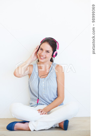 Music, portrait and headphones for woman on a floor in studio, happy and streaming on a wall background. Face, smile and girl relax with podcast, radio or audio track while sitting against mockup 98999369