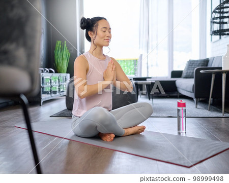 Prayer hands, yoga and meditation of Asian woman in home living room for mindfulness exercise. Zen chakra, pilates and female yogi training and meditating with namaste hand pose for relax and peace. 98999498