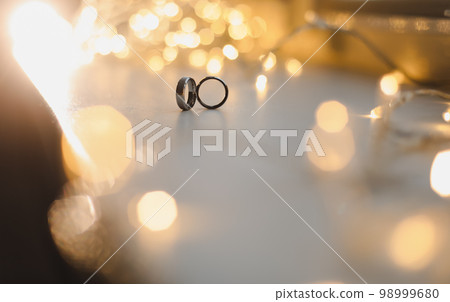 Wedding rings on blured bokeh glowing golden background. Symbol of love and romance on a textured glitter background with copy space for your greeting or congratulations 98999680