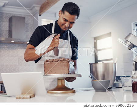 Piping, decorating and man baking a cake with chocolate in a kitchen or pastry chef happy with online recipe. Food, desert and cook preparing a sweet meal in Brazil and using a tablet 99003239