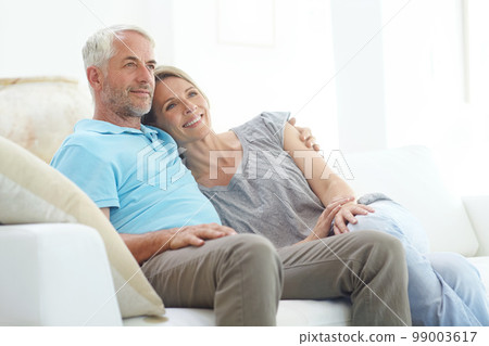 Senior couple, retirement and thinking on a couch at home with love, care and support from life insurance. Commitment of a man and woman in a healthy marriage with security on living room couch 99003617