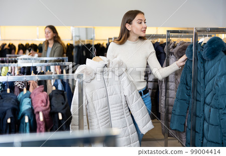 Young woman choosing insulated coat in store Young woman choosing insulated coat in store 99004414