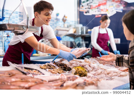 Positive salesman demonstrating red snapper to purchaser in fish store 99004452