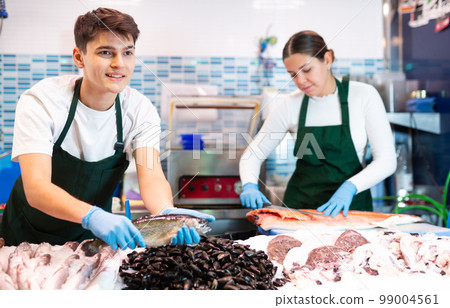 Responsive shop assistant in green apron demonstrating trout in fish store Responsive shop assistant in green apron demonstrating trout in fish store 99004561
