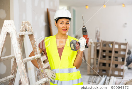 Smiling woman builder holding drill, repair works in apartment 99004572