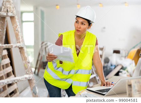 Female architect matching check list and using laptop during repair works Female architect matching check list and using laptop during repair works 99004581