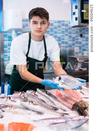 Smiling salesman demonstrating seabass in fish store 99004625