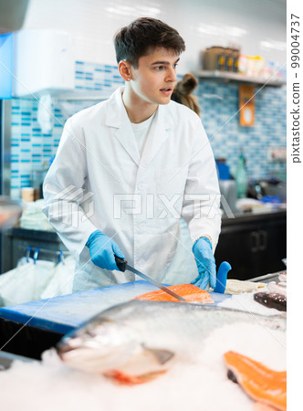 Proficient salesman cutting fish fillet in fish store 99004737