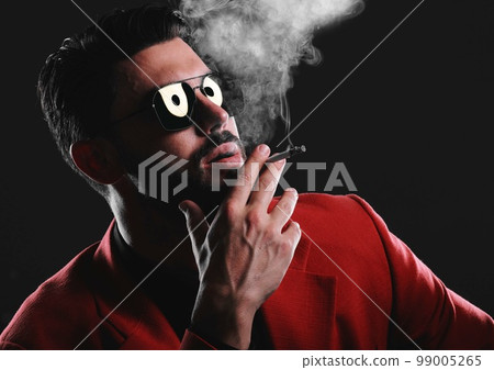Fashion, smoke and face with a man model in studio on a dark background wearing a suit for style. Smoking, mafia and edgy with a handsome young male posing on black space holding a cigarette 99005265