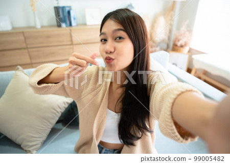 Pretty young asian female with big smile sitting at living room Pretty young asian female with big smile sitting at living room 99005482
