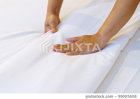 Female Hand set up white bed sheet in bedroom or maid hands making bed in a hotel room 99005608