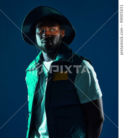 Fashion, shadow and black man model in a studio with a cool, stylish and casual outfit with lighting. Edgy, style and trendy fashionable African male posing while isolated by a blue background. Fashion, shadow and black man model in a studio with a cool, stylish and casual outfit with lighting. Edgy, style and trendy fashionable African male posing while isolated by a blue background. 99005831