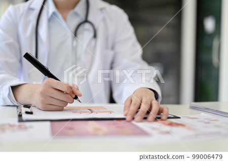 Cropped image or a professional Asian female doctor in white gown working on medical report 99006479