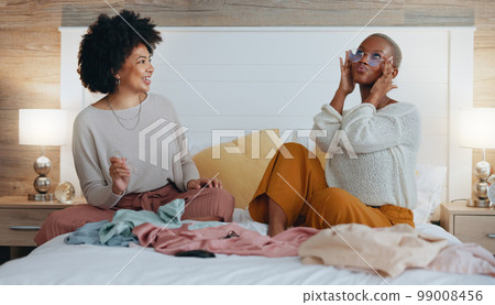 Fashion, bedroom and friends choosing clothing for girls night out. Happy, smile and black woman on bed with friend sharing clothes. Women help with outfit choice for interview, social event or date. Fashion, bedroom and friends choosing clothing for girls night out. Happy, smile and black woman on bed with friend sharing clothes. Women help with outfit choice for interview, social event or date. 99008456
