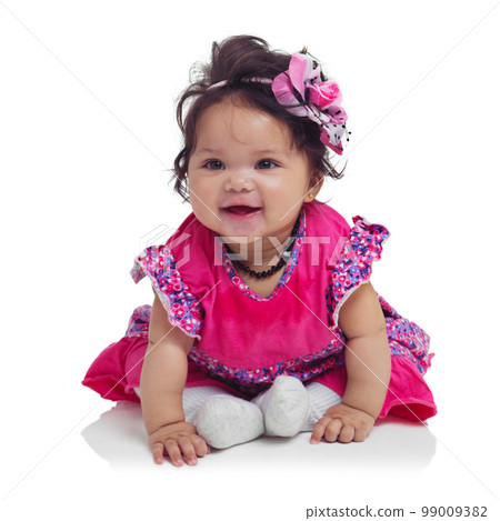 Innocent, cute and happy baby girl in a studio with a floral, beautiful and flower outfit and headband. Happiness, smile and infant child sitting and playing while isolated by a white background. 99009382