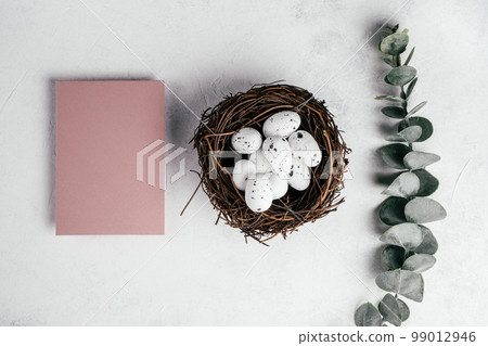 Easter composition of pink blank empty postcard on white background and quail eggs in nest near branch of eucalyptus Easter composition of pink blank empty postcard on white background and quail eggs in nest near branch of eucalyptus 99012946