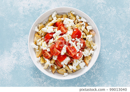 Dakos or koukouvagia salad. Classic recipe Cretan barley rusk salad with fresh tomato, mizithra cheese and oregano. Traditional mediterranean Greek cuisine. Healthy food, diet. Top view Dakos or koukouvagia salad. Classic recipe Cretan barley rusk salad with fresh tomato, mizithra cheese and oregano. Traditional mediterranean Greek cuisine. Healthy food, diet. Top view 99013040