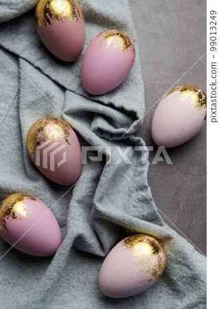 Easter eggs are painted with violet and gold paint on a gray linen background. Easter eggs are painted with violet and gold paint on a gray linen background. 99013249