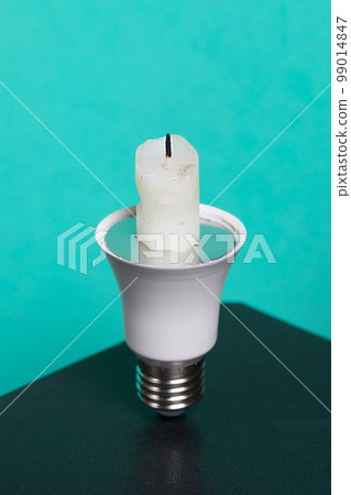 Light bulb with candle stub. Global ecology, International Energy Saving Day or Earth Hour concept. On a turquoise background. Light bulb with candle stub. Global ecology, International Energy Saving Day or Earth Hour concept. On a turquoise background. 99014847