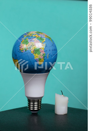 Light bulb with Earth planet model with space for text. Nearby is a candle stub. Global ecology, International Day of Energy Saving or Earth Hour concept. On a turquoise background. 99014886