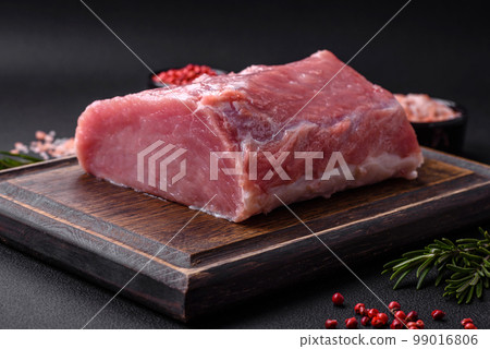 A piece of raw fresh pork on a wooden cutting board with spices and herbs 99016806