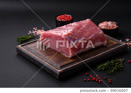 A piece of raw fresh pork on a wooden cutting board with spices and herbs 99016807