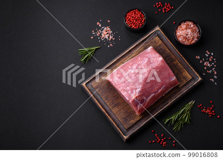 A piece of raw fresh pork on a wooden cutting board with spices and herbs 99016808