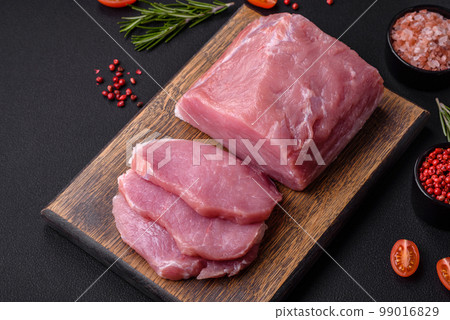 A piece of raw fresh pork on a wooden cutting board with spices and herbs A piece of raw fresh pork on a wooden cutting board with spices and herbs 99016829