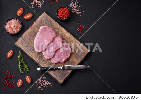 A piece of raw fresh pork on a wooden cutting board with spices and herbs A piece of raw fresh pork on a wooden cutting board with spices and herbs 99016839
