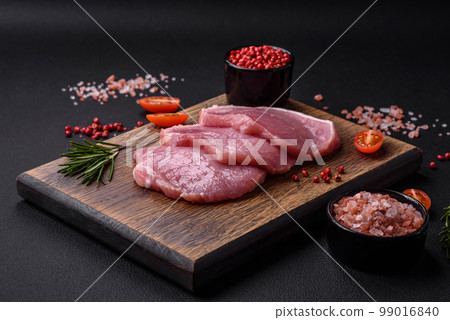 A piece of raw fresh pork on a wooden cutting board with spices and herbs A piece of raw fresh pork on a wooden cutting board with spices and herbs 99016840
