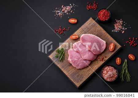 A piece of raw fresh pork on a wooden cutting board with spices and herbs 99016841