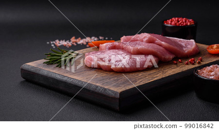 A piece of raw fresh pork on a wooden cutting board with spices and herbs A piece of raw fresh pork on a wooden cutting board with spices and herbs 99016842
