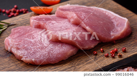 A piece of raw fresh pork on a wooden cutting board with spices and herbs 99016846