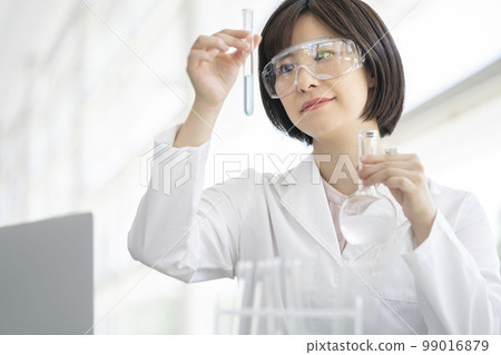 A woman in a white coat doing an experiment 99016879