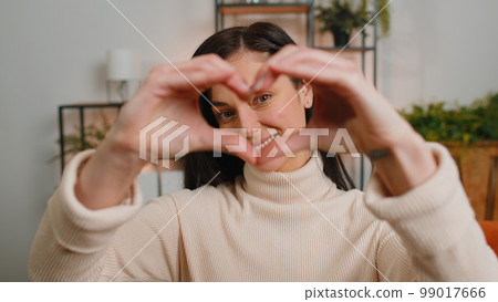Happy young woman girl makes symbol of love showing heart sign to camera express romantic feelings 99017666