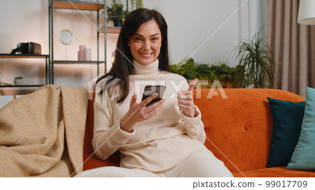 Happy young woman at home use smartphone typing browsing wow yes found out great big win celebrate Happy young woman at home use smartphone typing browsing wow yes found out great big win celebrate 99017709