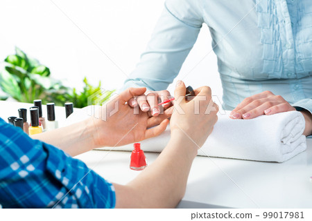Manicurist working with client's nails at table 99017981