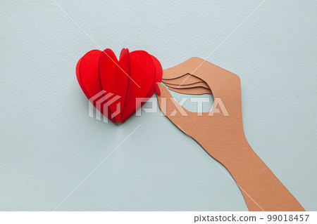 Handmade cutout heart in hand with manicure on blue background. Handmade cutout heart in hand with manicure on blue background. 99018457