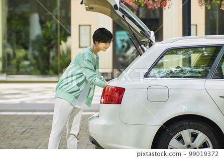 一個女人打開她的汽車的艙門並拿走行李 一個女人打開她的汽車的艙門並拿走行李 99019372