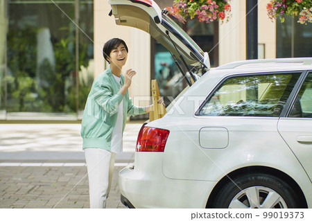 一個女人打開她的汽車的艙門並拿走行李 99019373