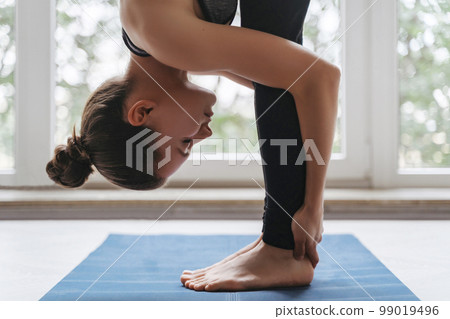 Attractive fit female practicing yoga with head to knees exercise Attractive fit female practicing yoga with head to knees exercise 99019496