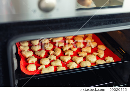 Sweet tasty delicious curd ginger cookies baking in hot oven stove on tray and red bright silicone bakery mat at home kitchen. Homemade hot biscuits making process 99020533