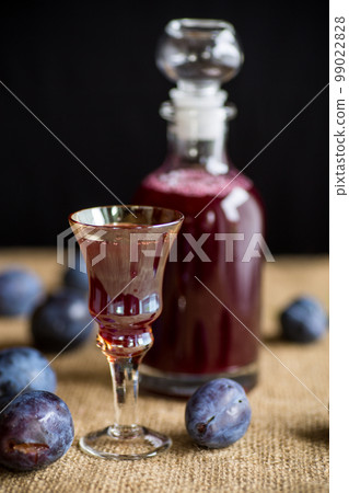 plum red wine in a glass and a decanter against the background of ripe large plums 99022828