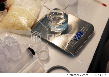 A laboratory view of beakers on electronic scales, beeswax and empty containers. 99023094