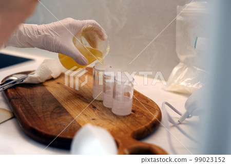 Hand pouring solution from laboratory beaker into empty container 99023152