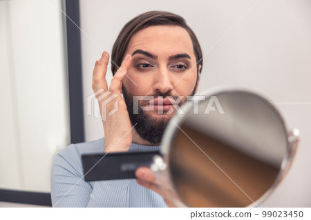 Male looking at himself in the mirror during makeup application 99023450