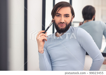 Transgender person powdering his face in the bathroom 99023455