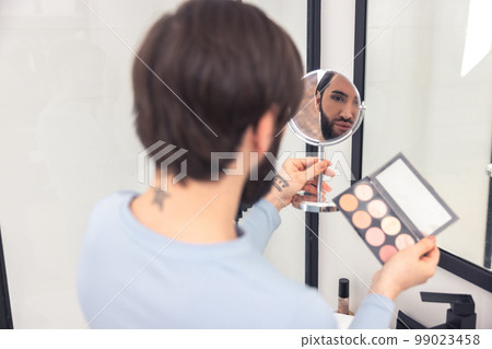 Focused guy examining his face after the blush application Focused guy examining his face after the blush application 99023458