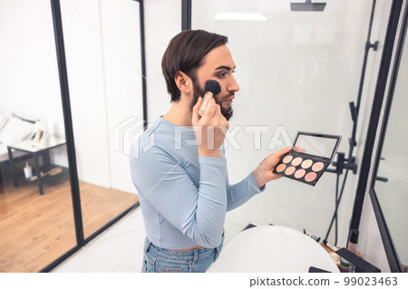 Young man applying rouge to his face 99023463