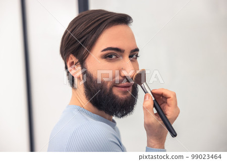 Transgender person applying powder to the face 99023464